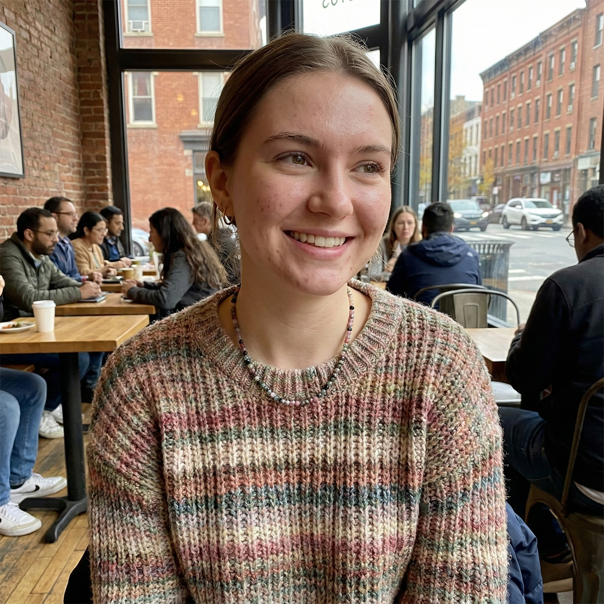 Woman smiling in a cafe with brick walls and large windows.