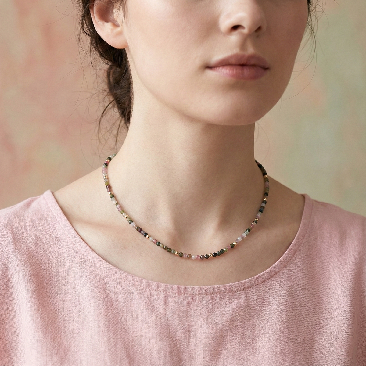 Person wearing a beaded necklace with a soft pink top against a blurred background