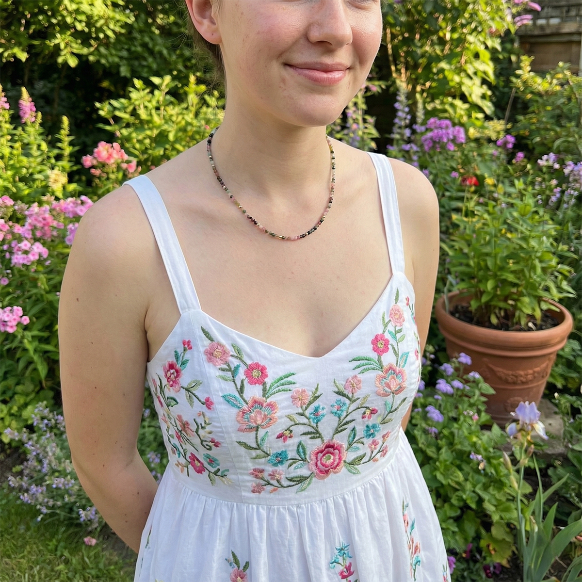 Person wearing a white dress with floral embroidery in a garden setting