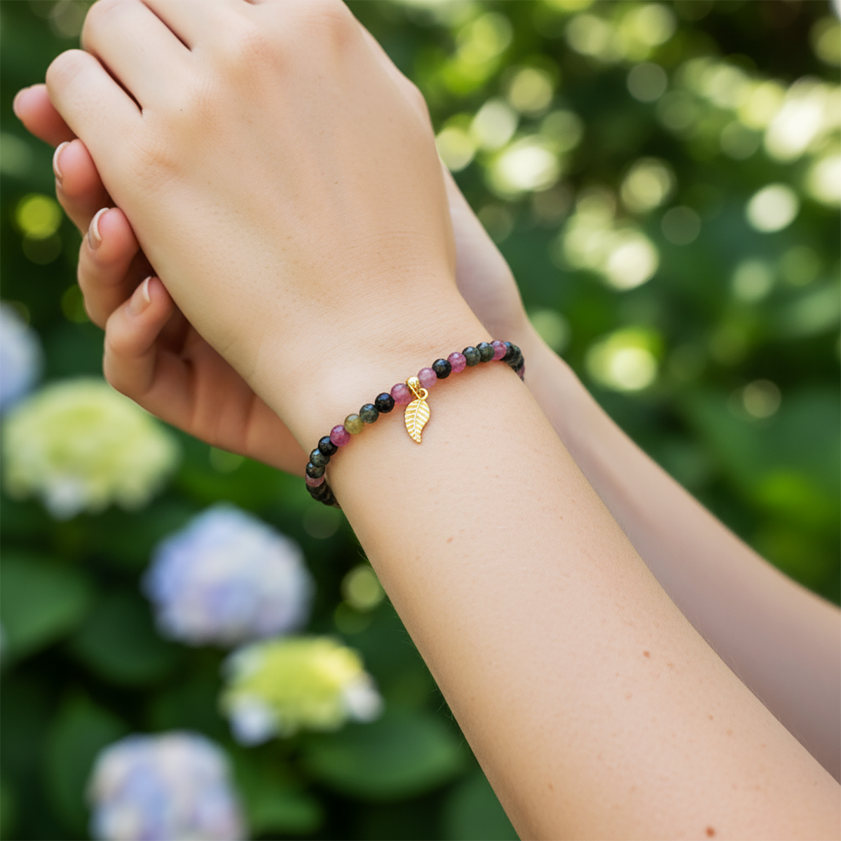 Hand wearing a beaded bracelet with a gold leaf charm against a blurred natural background