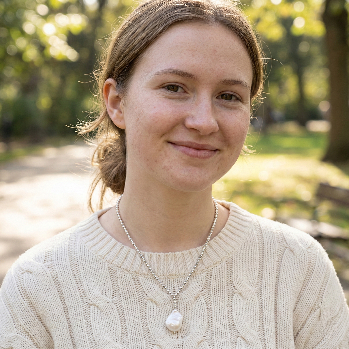 Woman wearing a beige sweater with a blurred park background