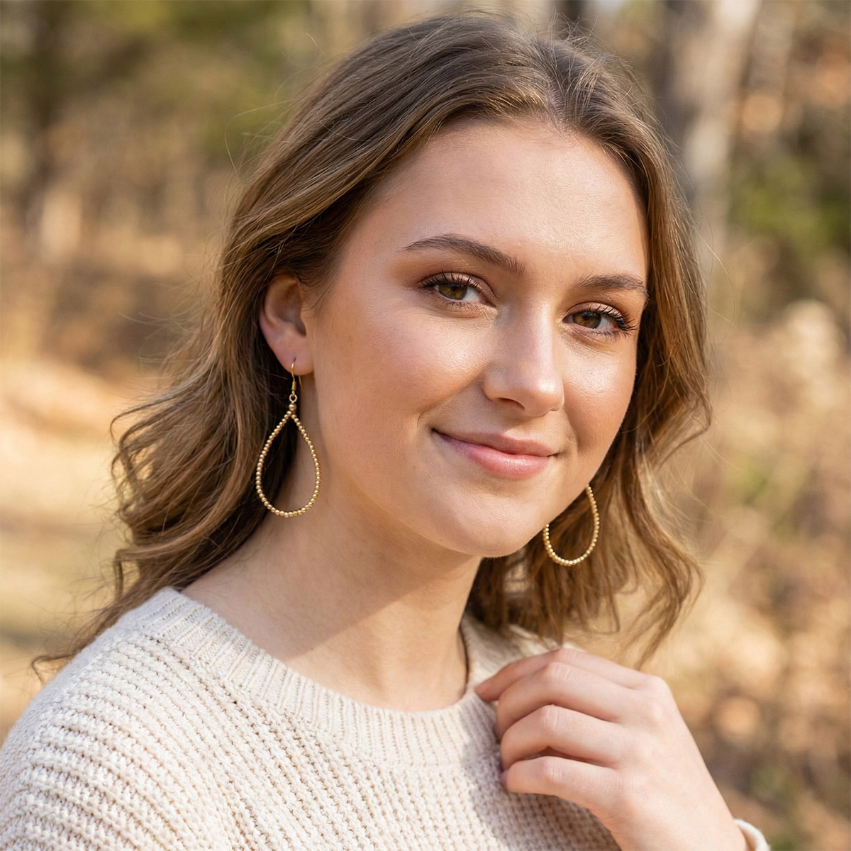 Woman with gold hoop earrings standing outdoors with a blurred natural background