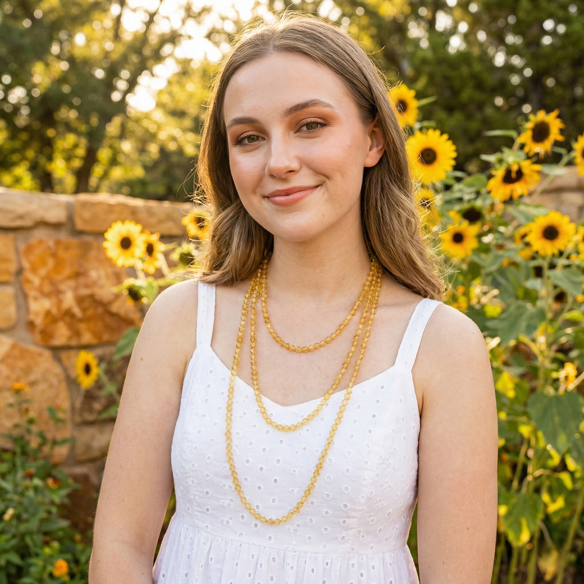 Woman in a white dress with gold necklaces standing in front of sunflowers