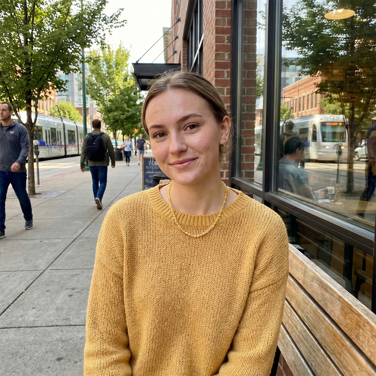 Woman in a yellow sweater sitting on a bench outdoors with a city street background