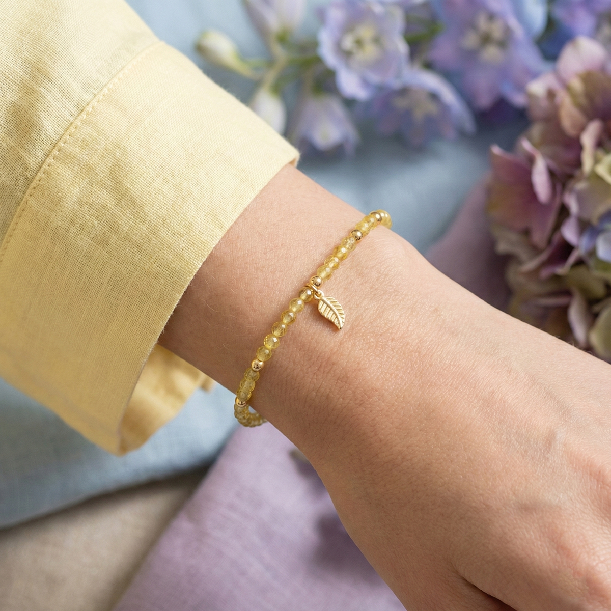 Gold bracelet on a wrist with a blurred floral background