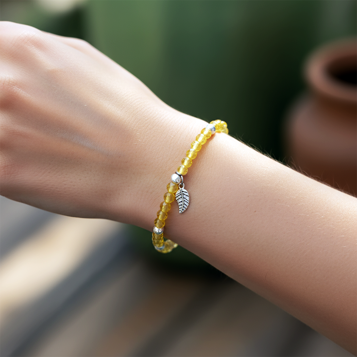 Yellow beaded bracelet with a leaf charm on a wrist against a blurred natural background