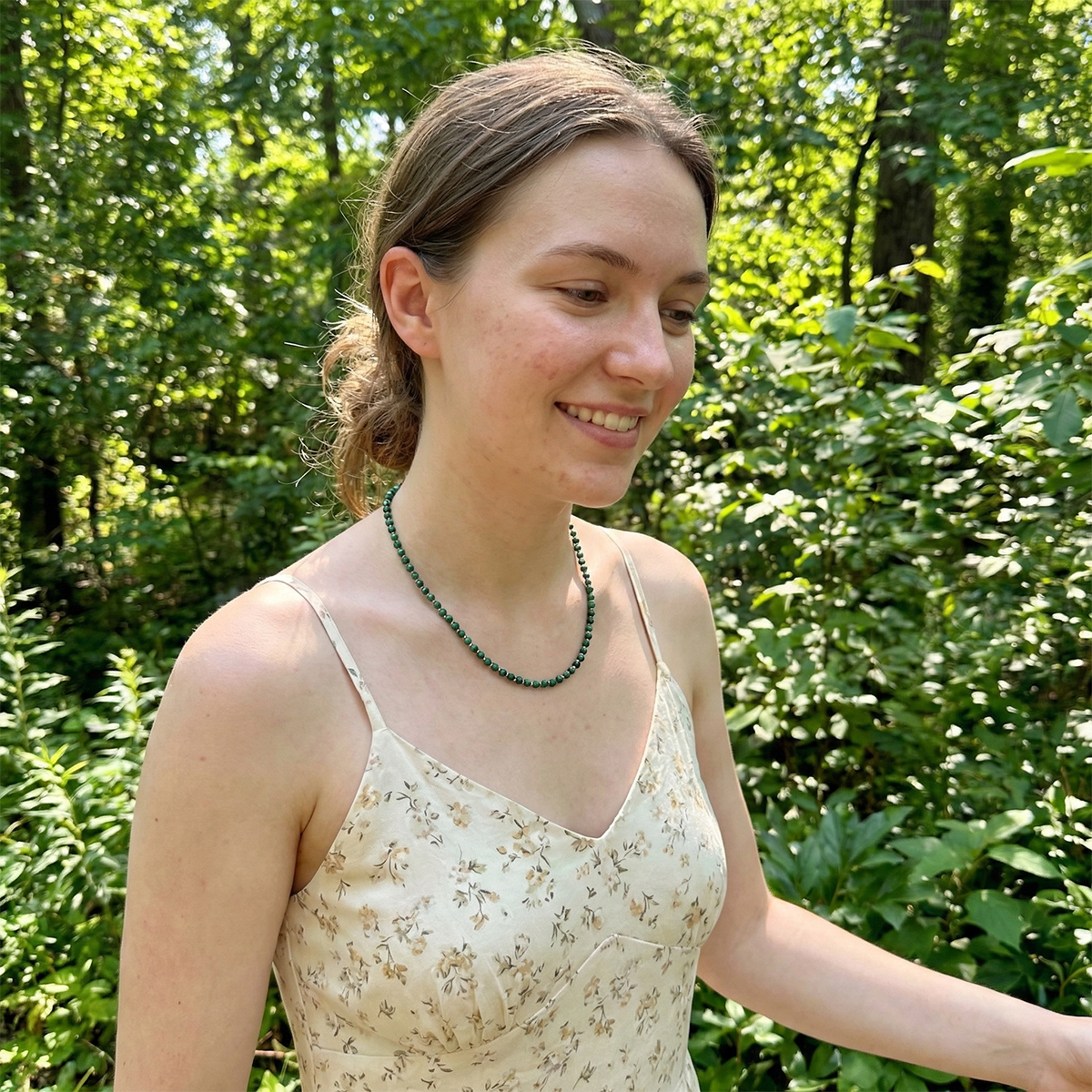 Woman in a floral dress with a green necklace standing in a forest