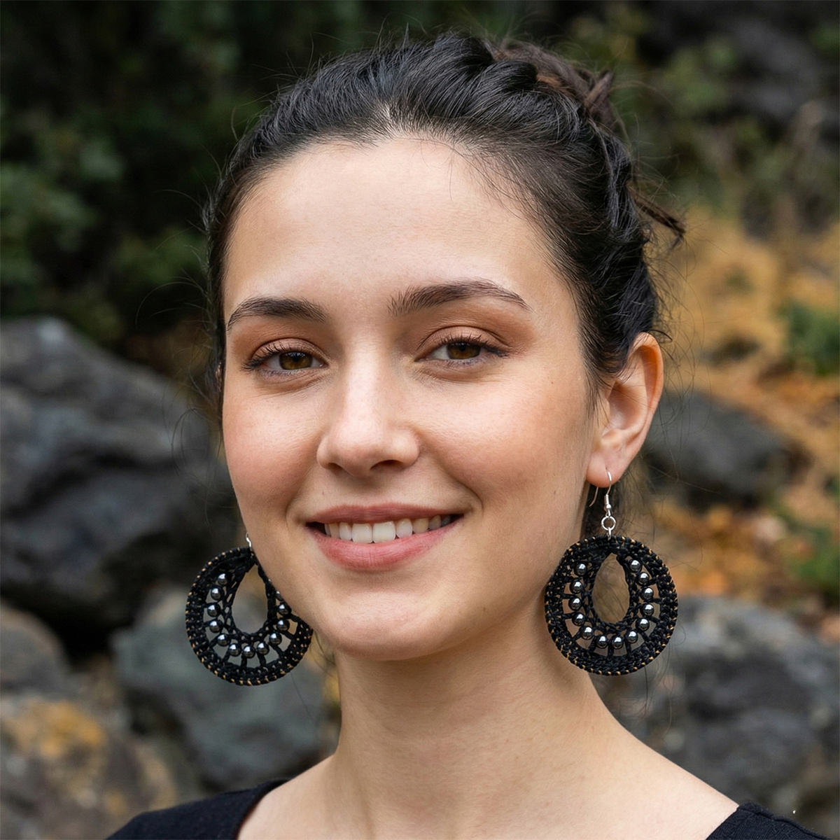 Woman wearing large black earrings with a natural background