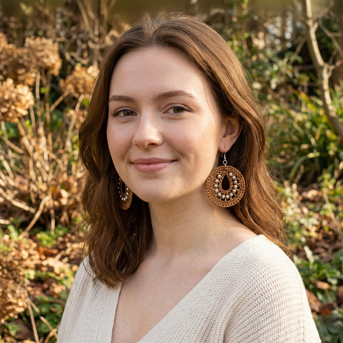 Woman with large earrings standing outdoors with greenery in the background