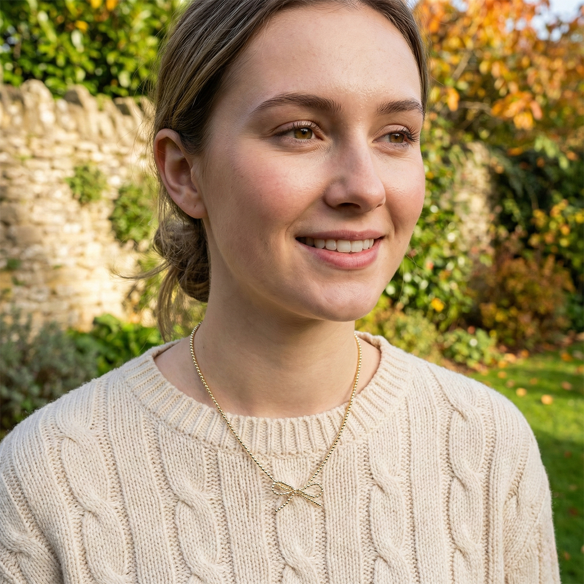 Woman wearing a beige sweater with a garden in the background