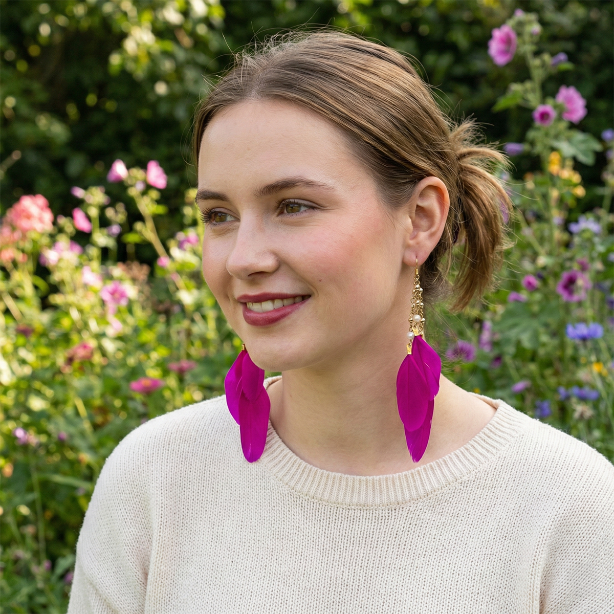 Woman wearing pink feather earrings outdoors with flowers in the background