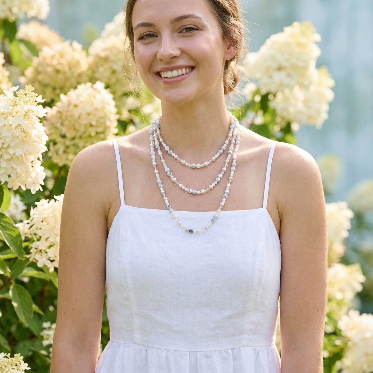 Woman wearing a white dress and pearl necklace in front of hydrangea flowers
