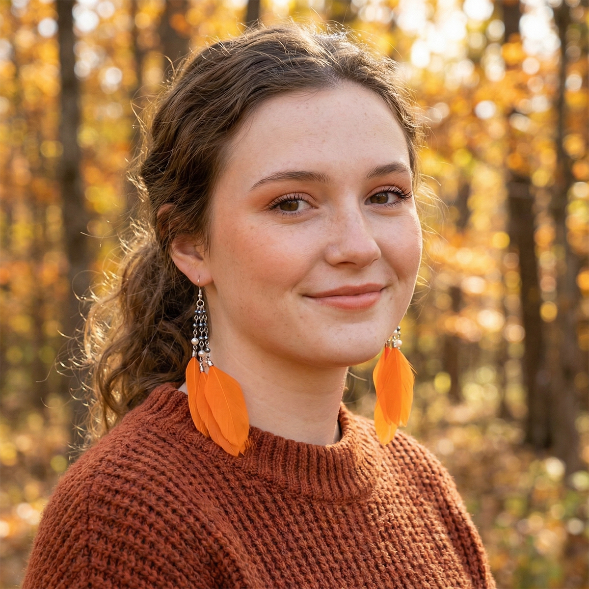 Woman wearing orange earrings and a brown sweater in an autumn forest