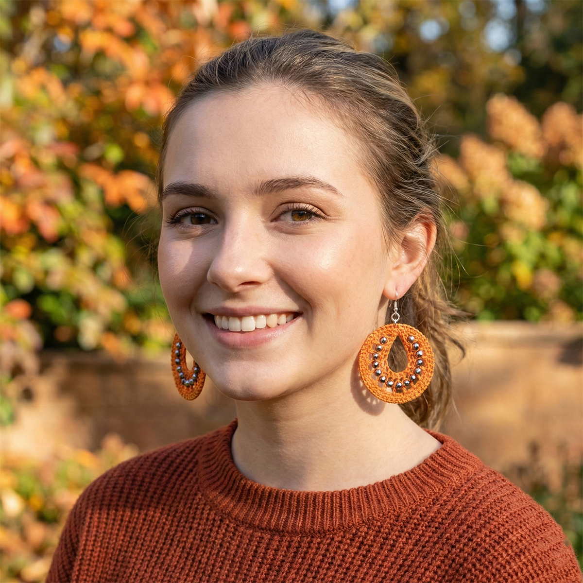 Woman wearing orange earrings with a blurred autumn background