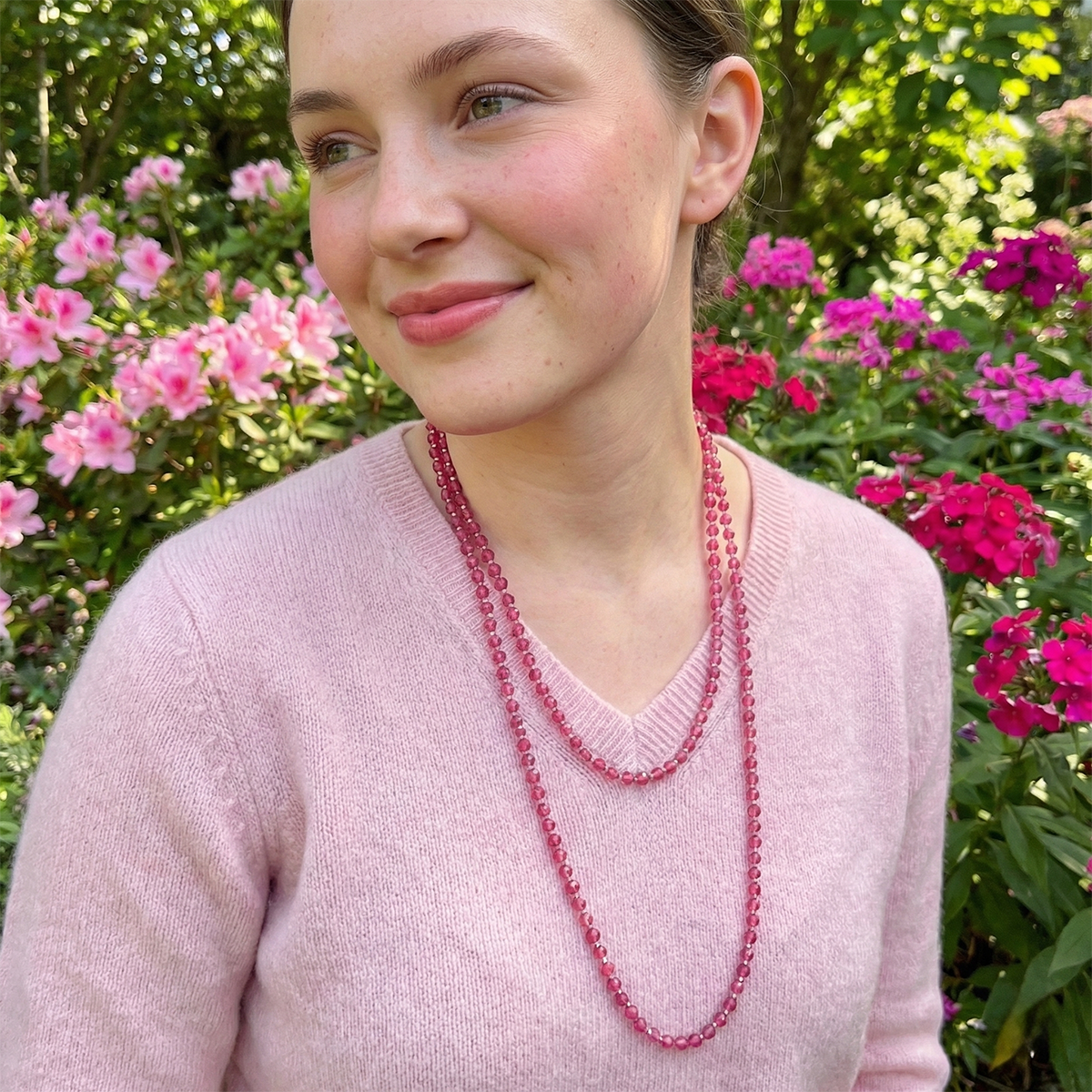 Woman wearing a pink sweater and red beaded necklace in front of pink flowers