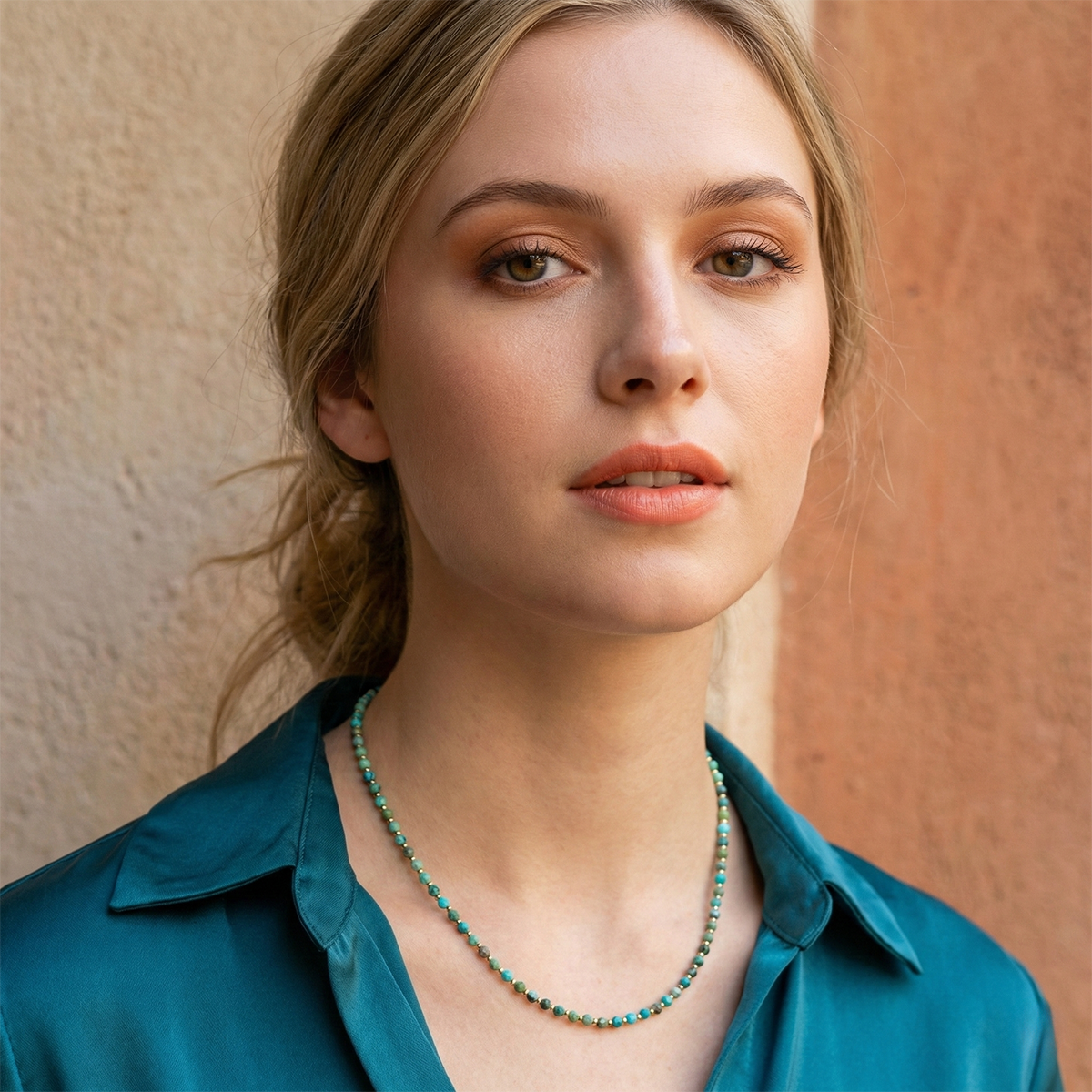 Woman wearing a teal shirt and necklace against a beige wall
