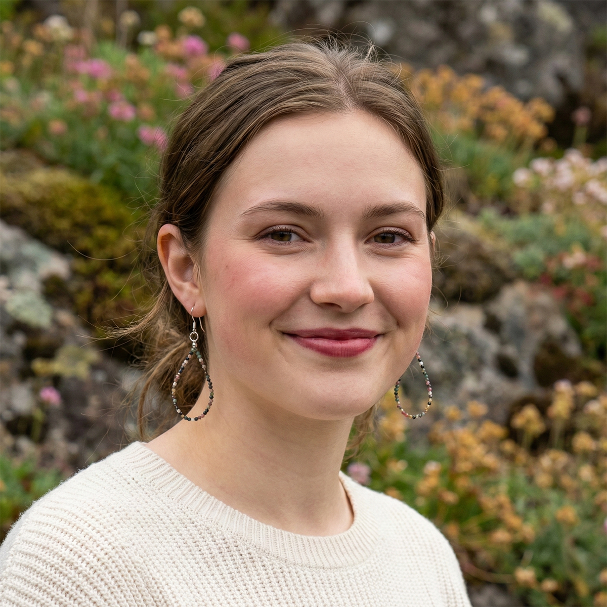 Woman with earrings standing in front of a natural background with rocks and flowers