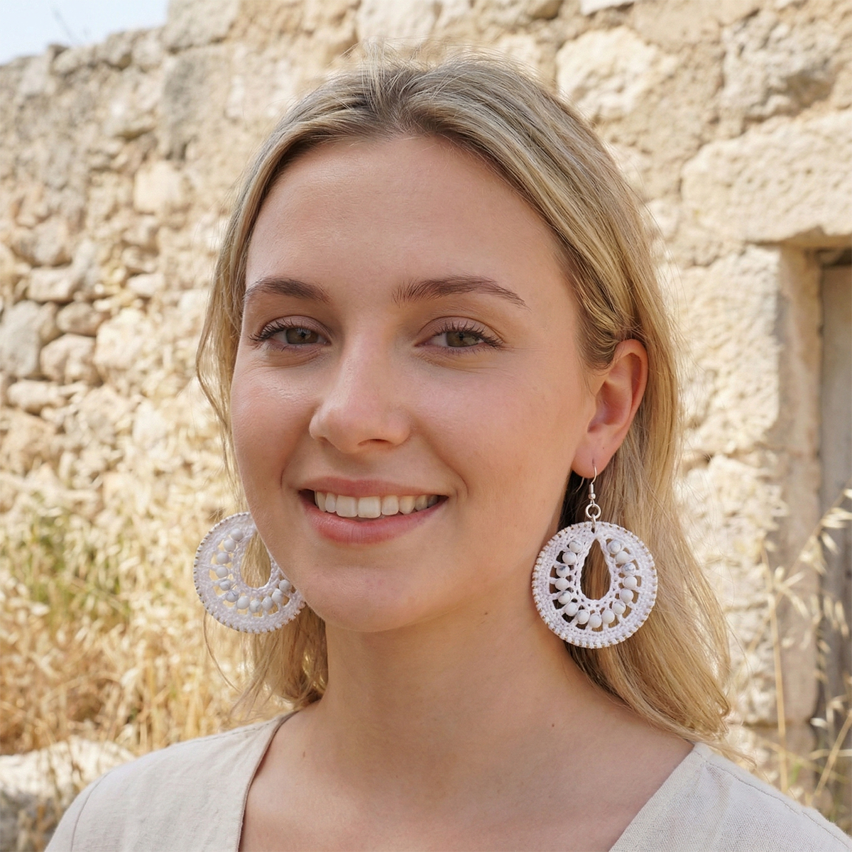 Woman wearing large, round, white earrings against a stone wall background