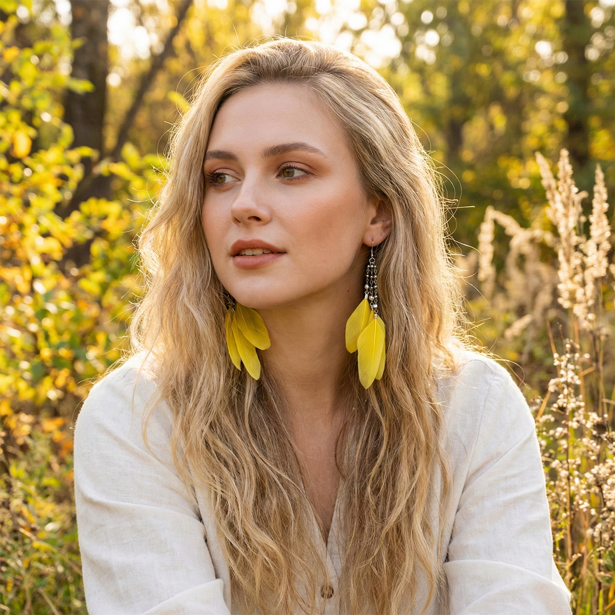 Woman with long blonde hair and yellow earrings standing in a natural setting.